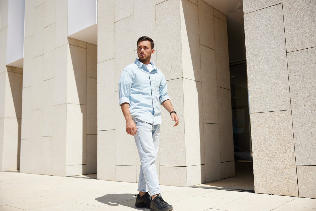 Man in light blue shirt and pants standing in front of a modern architectural building.